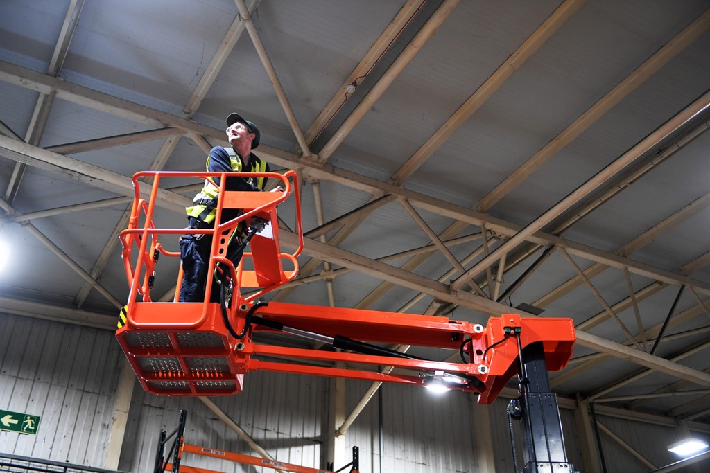 Operator working safely at height on a cherry picker inside a warehouse